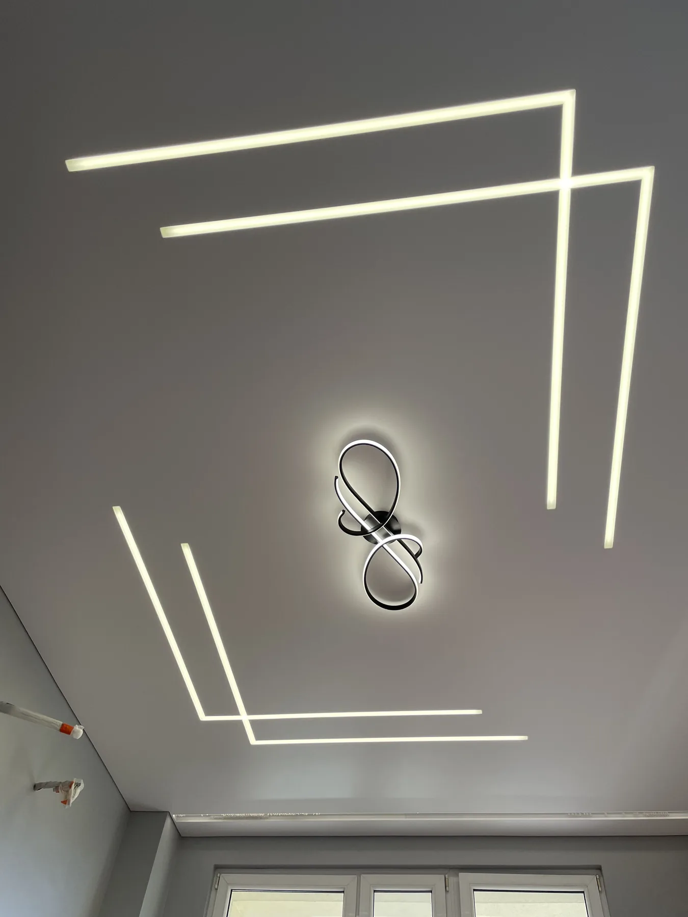 Jasny sufit napinany z czterema geometrycznymi liniami LED i ozdobną lampą pośrodku